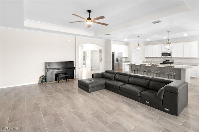 living area with arched walkways, a raised ceiling, visible vents, and crown molding