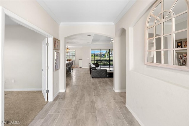 corridor featuring light wood-type flooring, baseboards, arched walkways, and crown molding