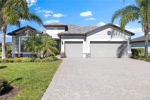 view of front facade featuring decorative driveway, stucco siding, a front yard, a garage, and stone siding