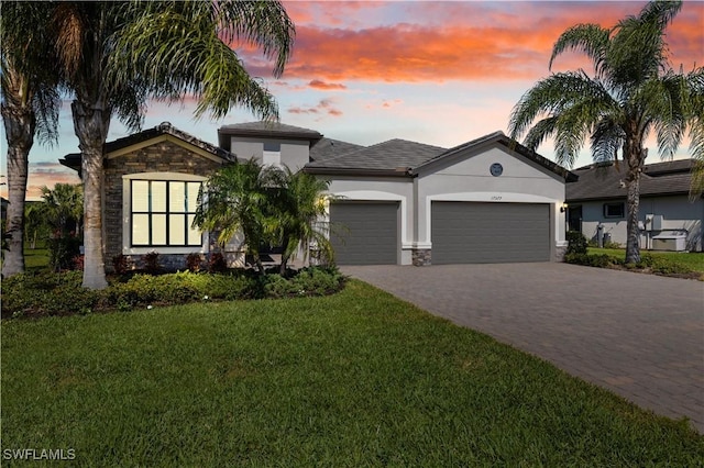 view of front of house featuring stone siding, an attached garage, decorative driveway, a yard, and stucco siding