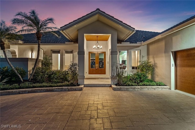 exterior entry at dusk featuring french doors, a tile roof, and stucco siding