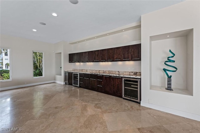 kitchen featuring dark brown cabinetry, wine cooler, baseboards, and light stone counters