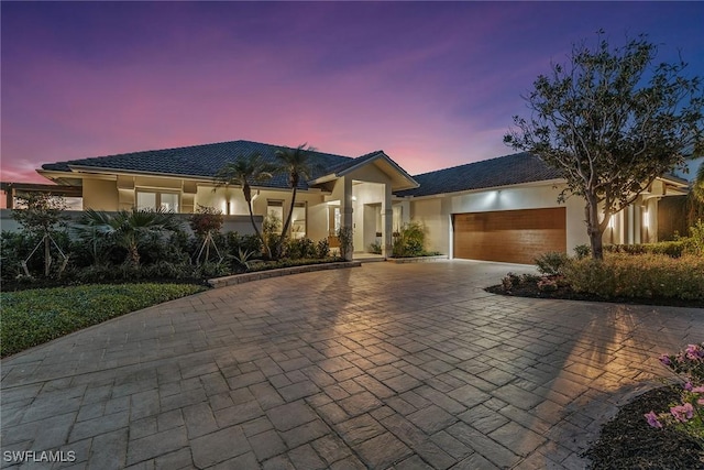 view of front of house with decorative driveway, an attached garage, and stucco siding