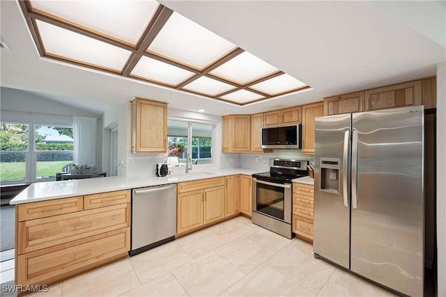 kitchen featuring appliances with stainless steel finishes, a peninsula, light countertops, light brown cabinets, and a sink