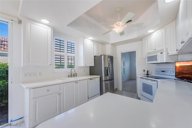 kitchen with a tray ceiling, white appliances, white cabinetry, and a sink