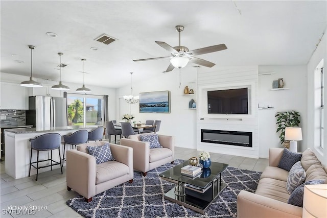 living area with ceiling fan with notable chandelier, a glass covered fireplace, visible vents, and wood tiled floor