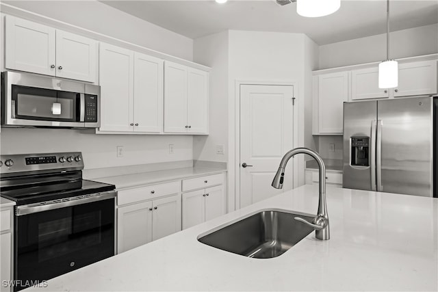 kitchen featuring white cabinetry, stainless steel appliances, a sink, and decorative light fixtures