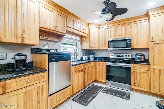 kitchen with light tile patterned floors, appliances with stainless steel finishes, a sink, ceiling fan, and dark stone counters