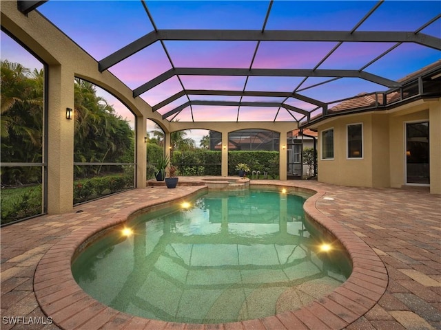 pool at dusk with glass enclosure, a pool with connected hot tub, and a patio