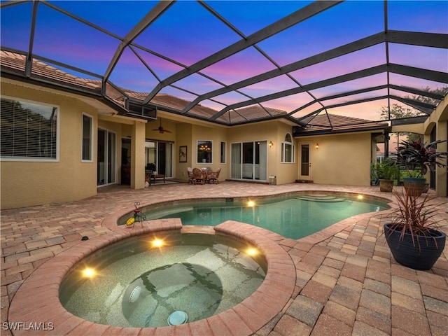 pool at dusk with a pool with connected hot tub, a patio area, ceiling fan, and a lanai