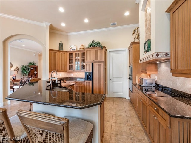 kitchen with arched walkways, a breakfast bar, a sink, wall chimney range hood, and black appliances