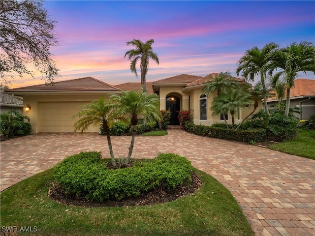 mediterranean / spanish-style home featuring a garage, decorative driveway, a tiled roof, and stucco siding