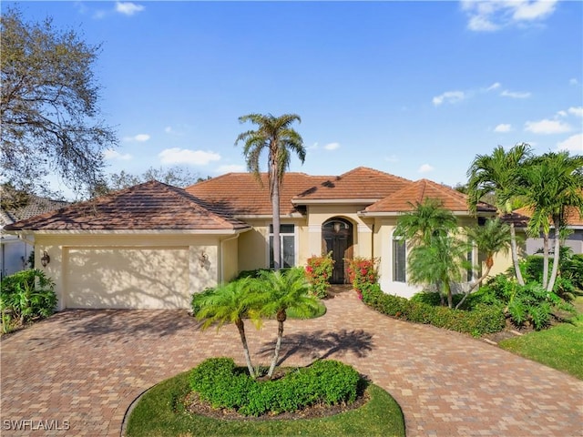 mediterranean / spanish home featuring decorative driveway, an attached garage, a tile roof, and stucco siding