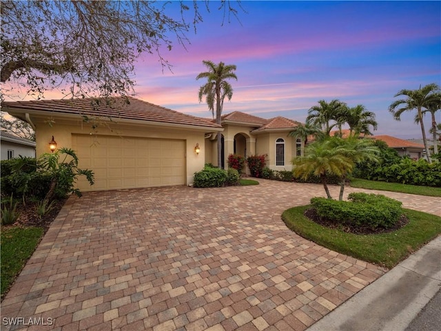 mediterranean / spanish-style home with a tiled roof, decorative driveway, an attached garage, and stucco siding