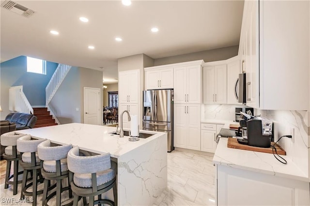 kitchen featuring white cabinetry, appliances with stainless steel finishes, light stone counters, and a sink