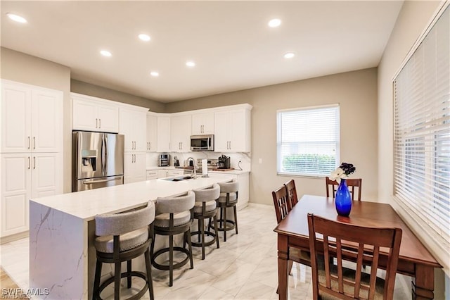 kitchen featuring recessed lighting, white cabinets, appliances with stainless steel finishes, an island with sink, and a kitchen bar