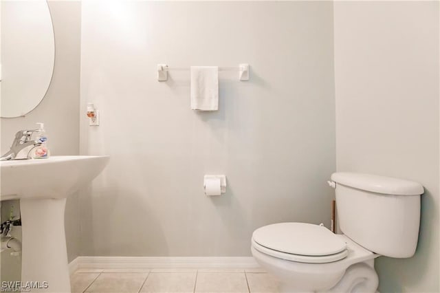 half bath featuring toilet, baseboards, a sink, and tile patterned floors