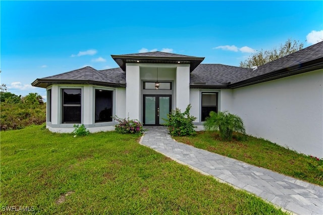 entrance to property featuring stucco siding, roof with shingles, a yard, and french doors