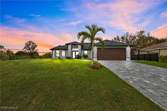 prairie-style house featuring a garage, decorative driveway, fence, and a front lawn