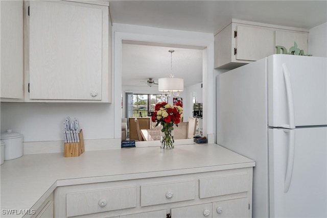 kitchen featuring freestanding refrigerator, light countertops, hanging light fixtures, and white cabinetry