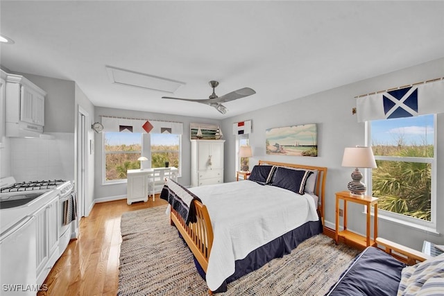 bedroom with light wood-style floors, attic access, baseboards, and a ceiling fan