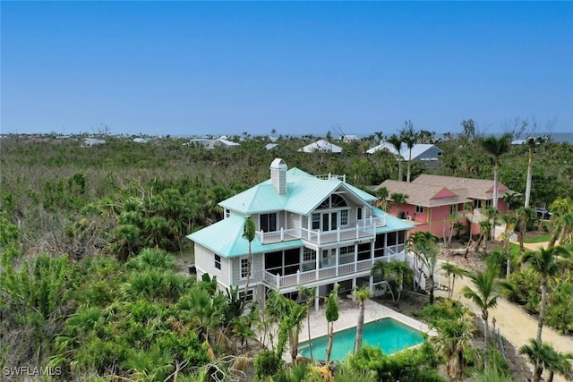 back of house featuring metal roof, a chimney, a balcony, and an outdoor pool