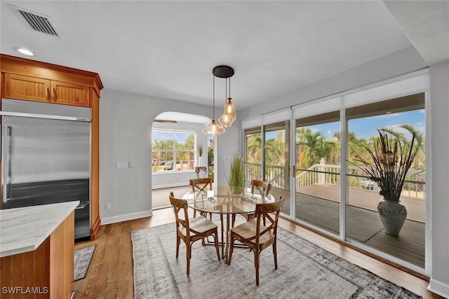 dining room with arched walkways, light wood-type flooring, visible vents, and baseboards