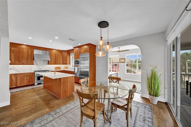 kitchen featuring built in appliances, a kitchen island, light countertops, wall chimney range hood, and decorative light fixtures