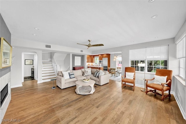 living area featuring light wood-style flooring, visible vents, a fireplace, and stairway