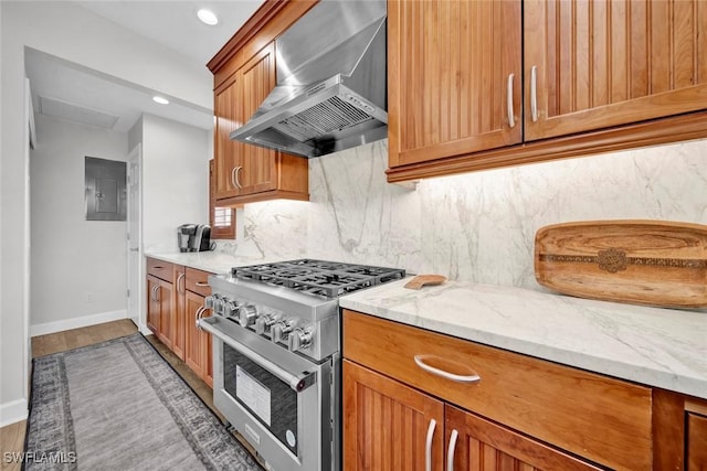 kitchen with wall chimney exhaust hood, light stone counters, decorative backsplash, and high end stainless steel range