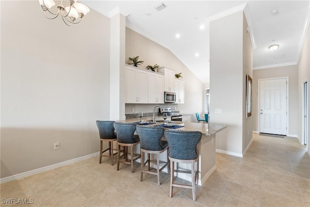 9365 Pocida Ct Unit 203, Naples, FL 34119 - kitchen with stainless steel appliances, white cabinets, crown molding, a breakfast bar area, and baseboards