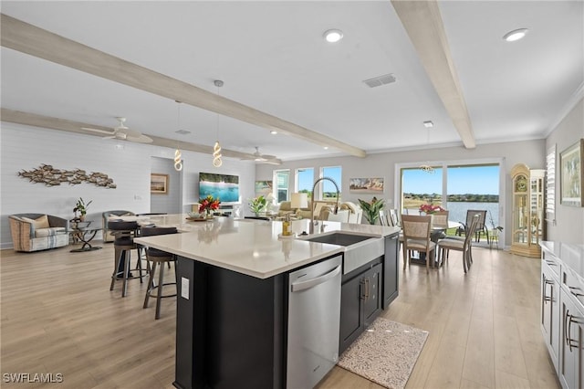 kitchen with a center island with sink, dishwasher, decorative light fixtures, light countertops, and beam ceiling