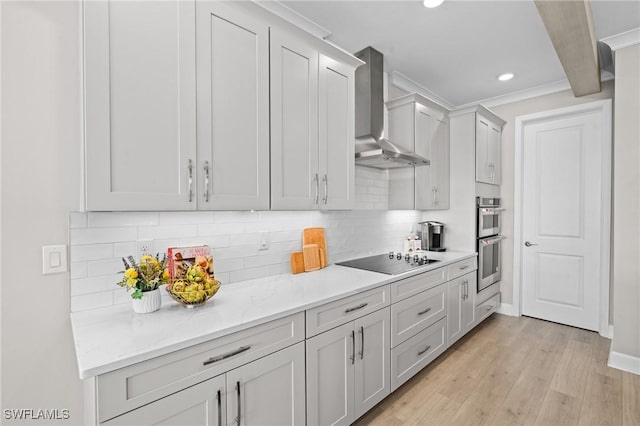 kitchen with decorative backsplash, wall chimney exhaust hood, black electric stovetop, stainless steel double oven, and light wood-style floors