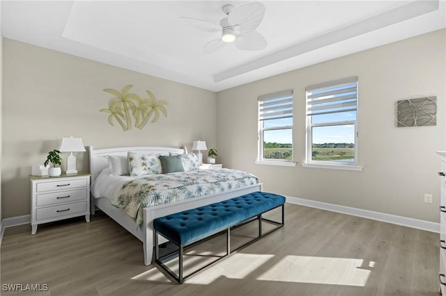 bedroom with light wood-type flooring, a tray ceiling, ceiling fan, and baseboards