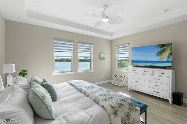 bedroom with light wood finished floors, baseboards, a raised ceiling, and a ceiling fan