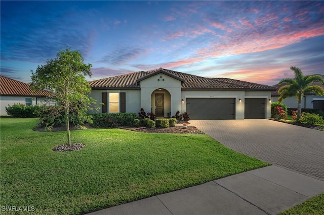 mediterranean / spanish home featuring decorative driveway, stucco siding, an attached garage, a tiled roof, and a front lawn