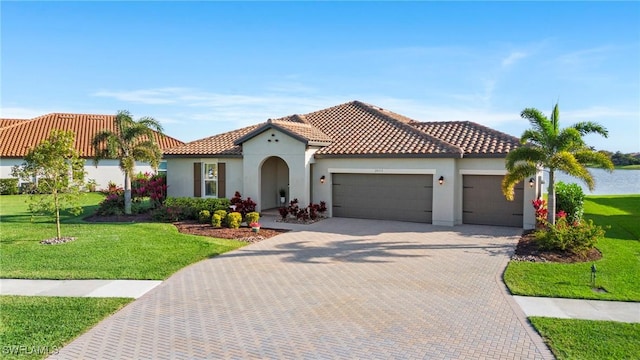 mediterranean / spanish-style house featuring a garage, stucco siding, decorative driveway, and a front yard