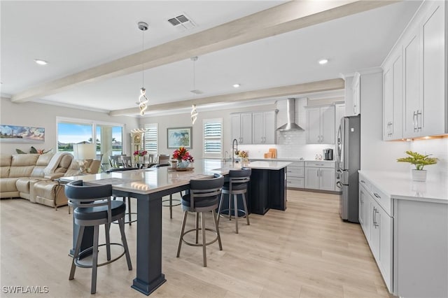 kitchen featuring open floor plan, light countertops, wall chimney range hood, and freestanding refrigerator