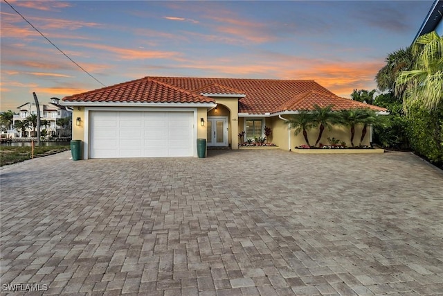 mediterranean / spanish-style house with a garage, decorative driveway, a tile roof, and stucco siding