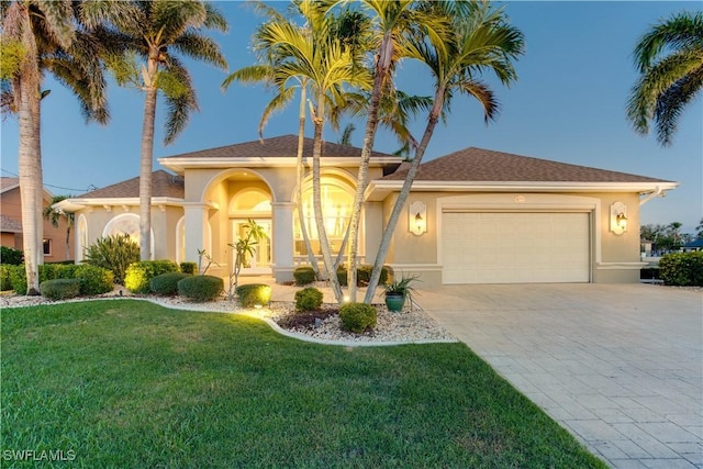 mediterranean / spanish house with decorative driveway, an attached garage, a front yard, and stucco siding