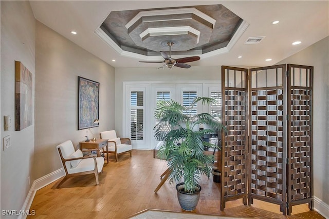 sitting room with a raised ceiling, visible vents, baseboards, and wood finished floors