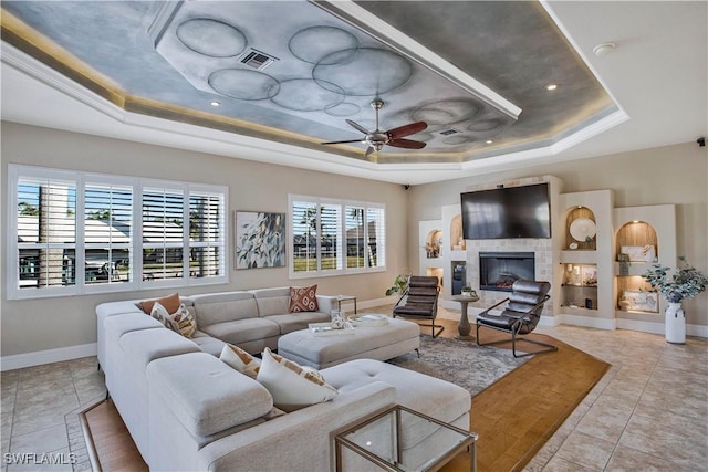 living area featuring light tile patterned floors, visible vents, a ceiling fan, a glass covered fireplace, and a tray ceiling