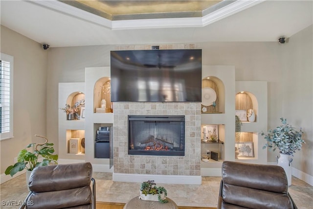 living room with a tiled fireplace, a raised ceiling, and baseboards