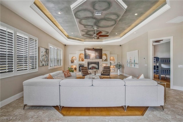 living area featuring a tray ceiling, a fireplace, visible vents, ceiling fan, and baseboards