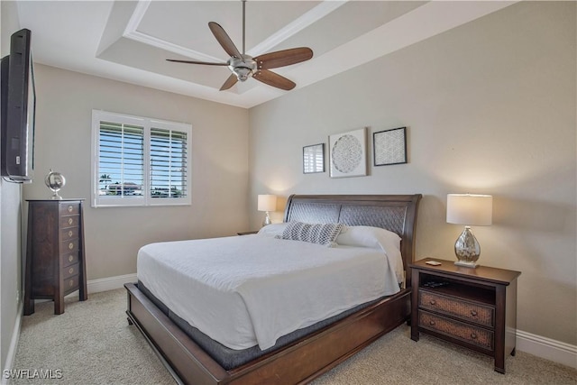 bedroom featuring light carpet, baseboards, a raised ceiling, and a ceiling fan