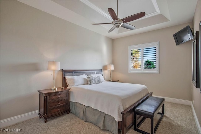 bedroom with a raised ceiling, light colored carpet, ceiling fan, and baseboards