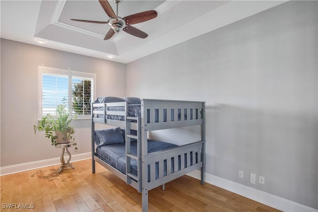 bedroom featuring a tray ceiling, wood finished floors, a ceiling fan, and baseboards