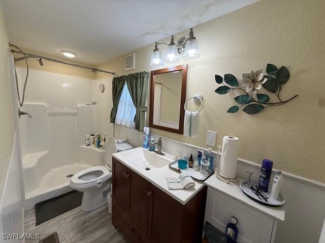 bathroom featuring visible vents, a textured wall, a shower stall, vanity, and wood finished floors