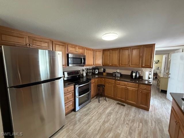 kitchen featuring appliances with stainless steel finishes, dark countertops, light wood-style floors, and brown cabinets