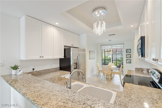 kitchen featuring stainless steel appliances, a sink, white cabinets, a tray ceiling, and an inviting chandelier